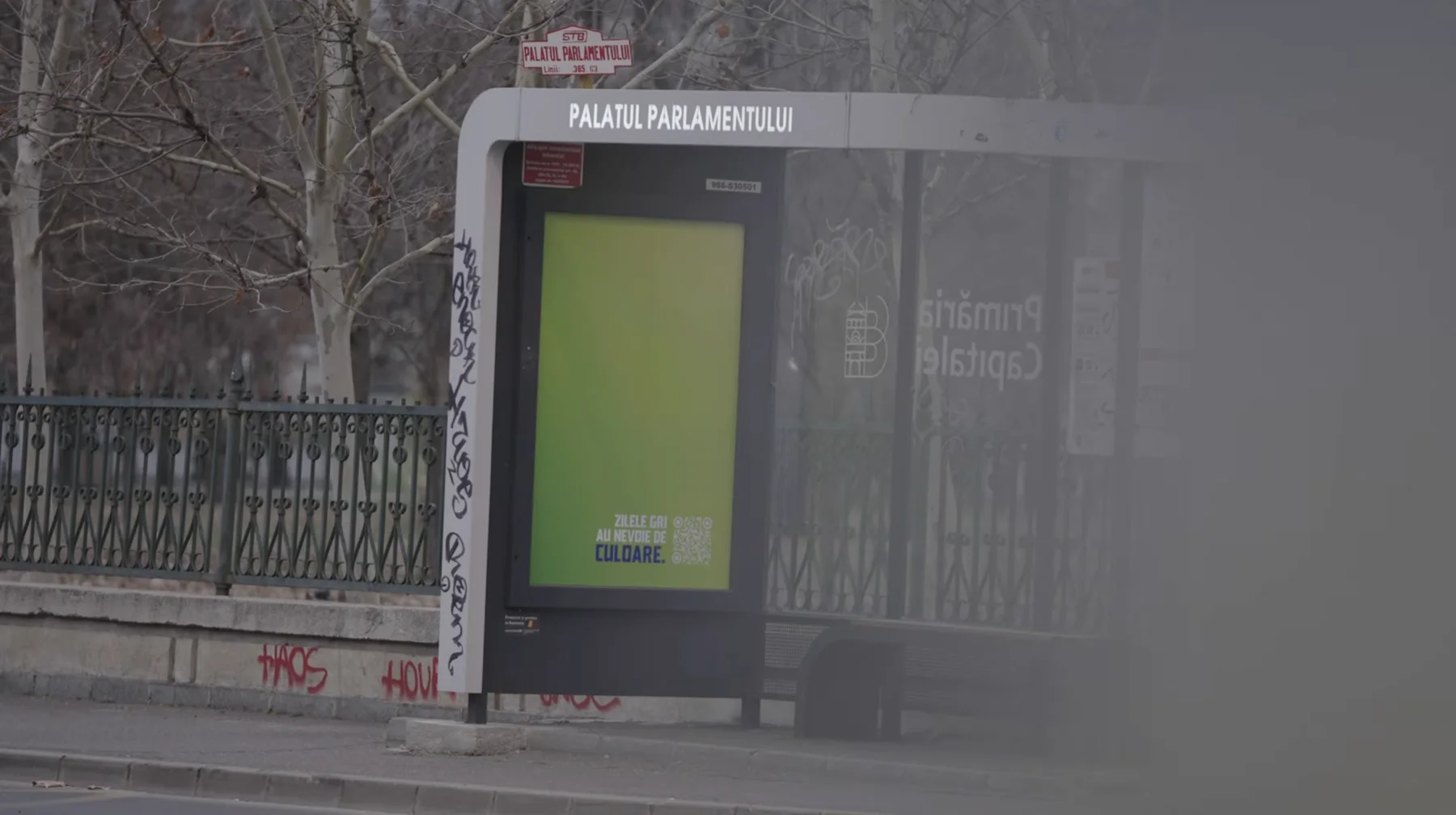 Bus shelter at Palatul Parlamentului with a green Fanta poster: grey days need colour.